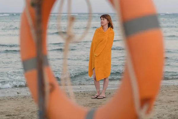 Un salvagente. Una ragazza in un asciugamano caldo si trova vicino al mare — Foto Stock