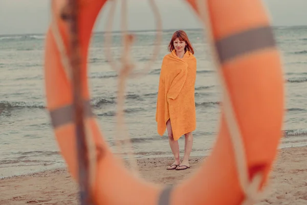 ライフブイ暖かいタオルをした少女が海の近くに立っている — ストック写真