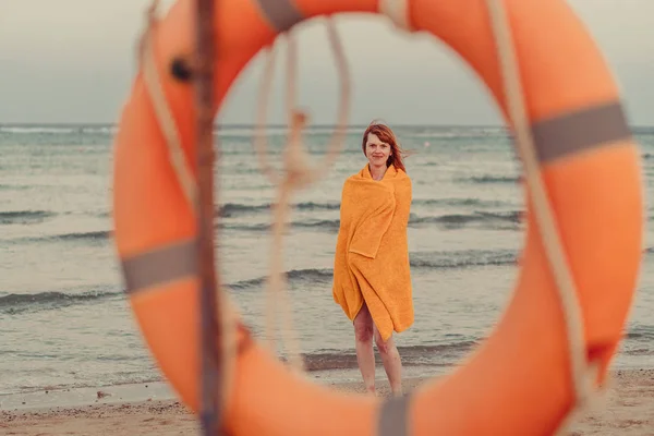 Un salvagente. Una ragazza in un asciugamano caldo si trova vicino al mare — Foto Stock