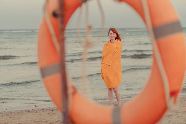 Un salvagente. Una ragazza in un asciugamano caldo si trova vicino al mare — Foto Stock