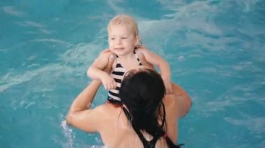 Yüzme havuzu. Annem küçük bir çocuğa havuzda yüzmeyi öğretiyor..