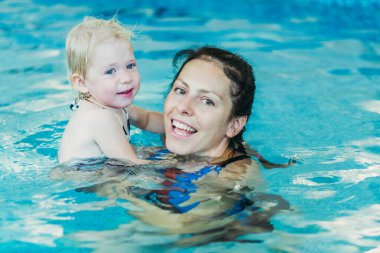 Yüzme havuzu. Annem küçük bir çocuğa havuzda yüzmeyi öğretiyor..