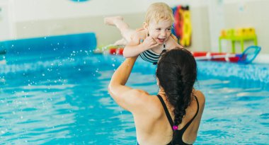 Yüzme havuzu. Annem küçük bir çocuğa havuzda yüzmeyi öğretiyor..