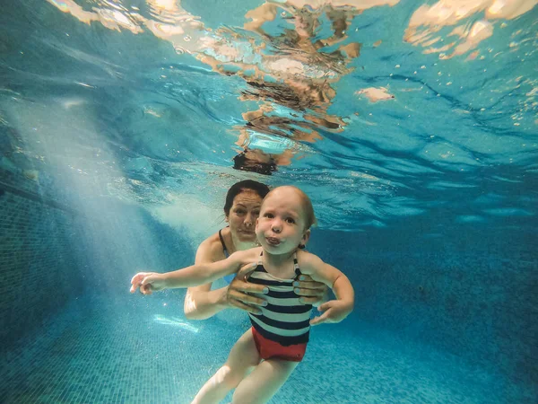 Zwembad. Moeder duikt met haar baby onder het zwembad water. — Stockfoto