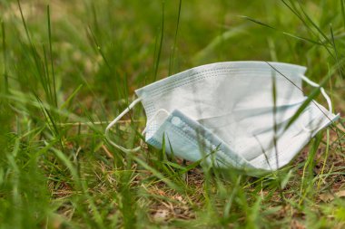 Tıbbi maske. Atılmış tıbbi maske yeşil bir çimenlikte yatıyor..