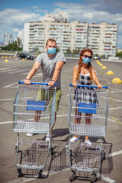 Supermarket trolley. A man and a woman wearing a medical mask are driving a supermarket trolley.