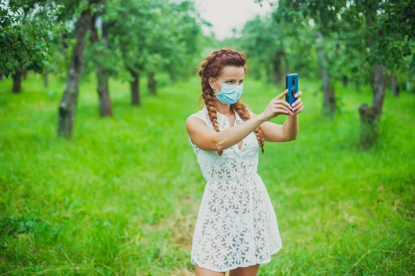 医疗面罩戴着医疗面罩的女人在智能手机上采花 — 图库照片