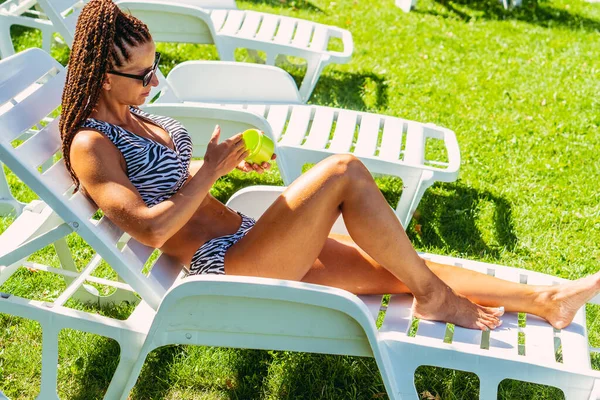 Bronzlaşmış. Mayolu bir kadın güneş kremi sürüyor..