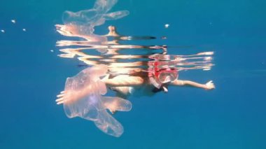 Virüs. Tıbbi bir eldiven, geçen bir kadının arka planına karşı denizde yüzer..