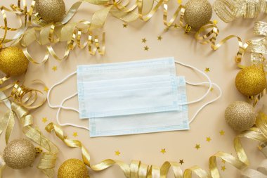 Altın konfeti, tıbbi maske, bant ve bej arka planda Noel oyuncak topları. Bayram arkaplanı. Corona virüsü covid-19 sırasında yeni yıl konsepti. Düz yatış, üst görünüm.