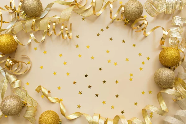Golden confetti, tape and Christmas toy balls on beige background. Festive holiday backdrop. Flat lay, top view, copy space.