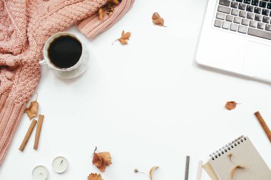 Örgü süveter, bir fincan kahve, dizüstü bilgisayar, defter, sonbahar yaprakları, tarçın çubukları, beyaz arka planda mumlar. Sonbahar kompozisyonu. Ofis masası çalışma alanı. Düz konum, üst görünüm, kopyalama alanı