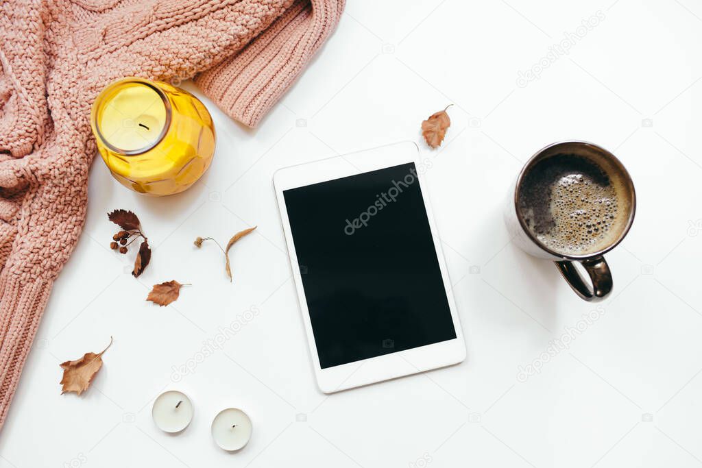 Knitted sweater, tablet, autumn leaves, candles on white background. Autumn composition. Flat lay, top view, copy space