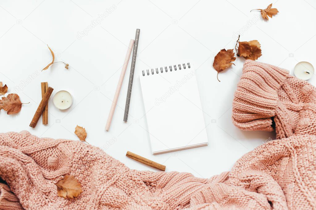 Knitted sweater, notebook, autumn leaves, cinnamon sticks, candles on white background. Autumn composition. Flat lay, top view, copy space
