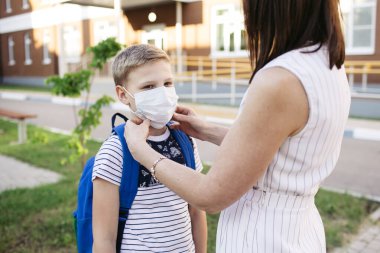 Anne, Covid-19 ya da Coronavirus salgınının okula hazırlanması için oğlunun yüzüne güvenlik maskesi takıyor. Okul konseptine geri dönelim. Koronavirüsü önlemek için tıbbi maske.
