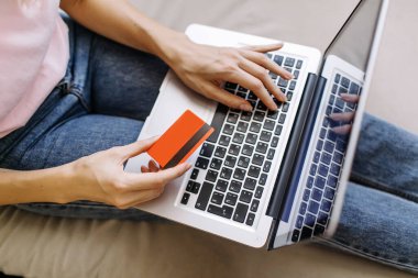 Kredi kartı tutan ve dizüstü bilgisayar kullanan bir kadın. İnternetten alışveriş