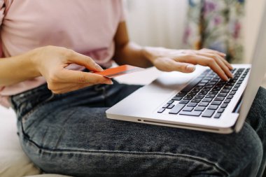 Kredi kartı tutan ve dizüstü bilgisayar kullanan bir kadın. İnternetten alışveriş