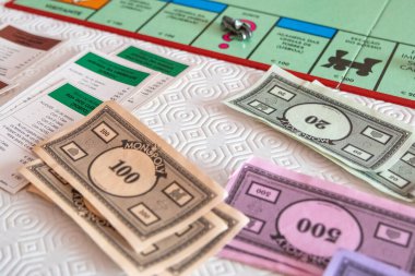 Monopoly oyunu parası ve emlak kartları bir oyun tahtasında, oyuncuların satın almaya ve satmaya başlaması için hazır.