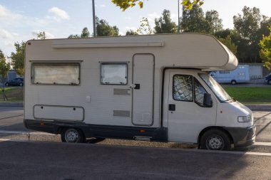 Arka planda ağaçlar olan bir şehir bölgesinde park edilmiş bir karavan.