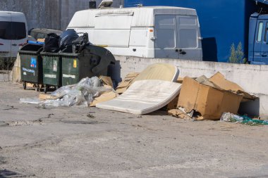 Çöpe atılmış yatak, karton kutular ve ıssız bir alanı kirleten plastik atık çevresel hasarı ve ihmali simgeliyor.