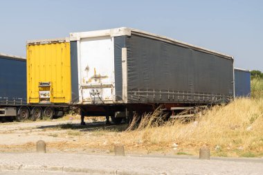 Detached semi trailers stand parked on dry grass under a clear blue sky, awaiting their next journey