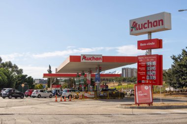 Cars queuing at an auchan energy gas station in alfragide, portugal, showing fuel prices and signage