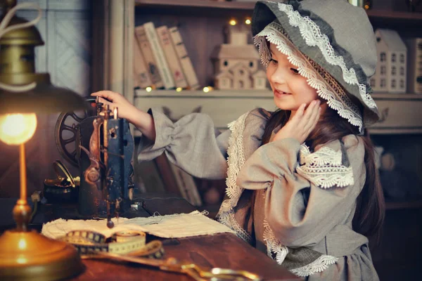 Belle petite fille dans une robe rétro avec une casquette coud sur une machine à coudre. Style rétro. Exécution . — Photo