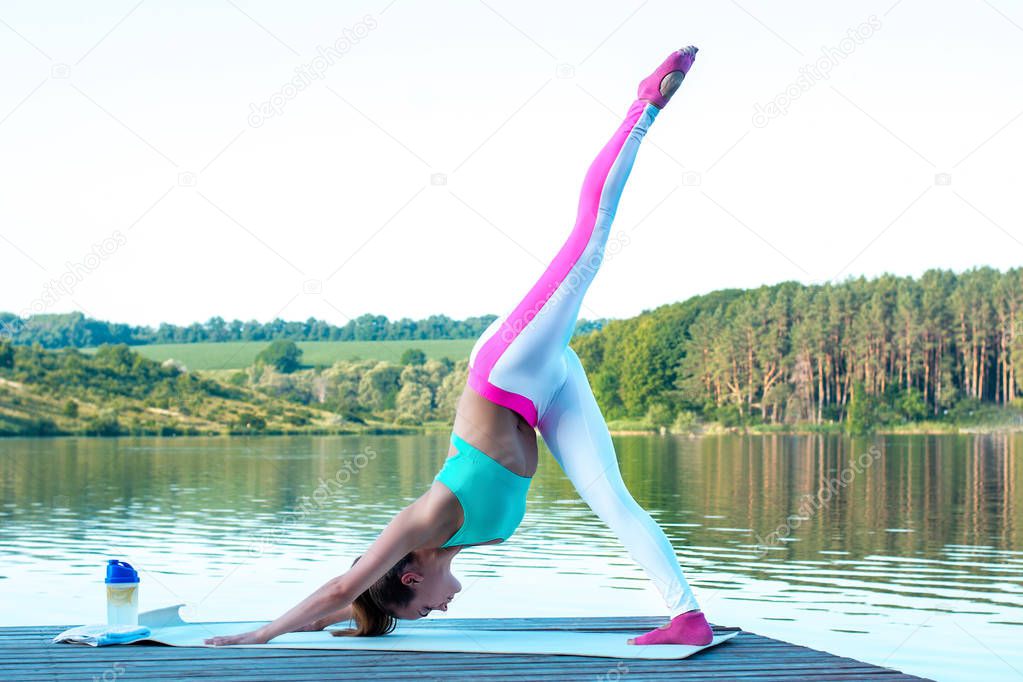 A beautiful girl on a background of beautiful nature makes an exercise pike, balancing on one leg. Health concept