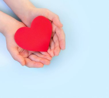 Çocukların elleri arka planda kırmızı kalbi tutar. Sağlık sigortası, organ bağışı, refah, aile sigortası, aşk dışında. Dünya Sağlık Günü. Ulusal Organ Bağışı Günü. Dünya Kalp Günü.