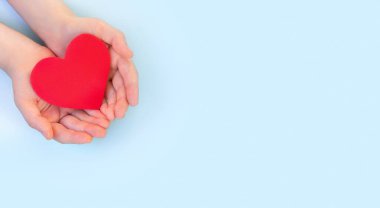 Çocukların elleri arka planda kırmızı kalbi tutar. Sağlık sigortası, organ bağışı, refah, aile sigortası, aşk dışında. Dünya Sağlık Günü. Ulusal Organ Bağışı Günü. Dünya Kalp Günü.
