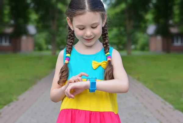 Yüzünde bir gülümseme olan güzel küçük kız sokaklarda akıllı saat kullanıyor.