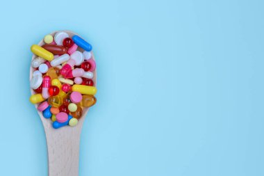 Renkli ilaç kapsülleri, tabletler ve mavi arka planda izole edilmiş tahta kaşıkta haplar. Beslenme takviyesi sağlık ürünleri. Metin için alanı kopyala.