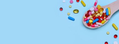 Renkli ilaç kapsülleri, tabletler ve mavi arka planda izole edilmiş tahta kaşıkta haplar. Beslenme takviyesi sağlık ürünleri. Metin için alanı kopyala. Banner