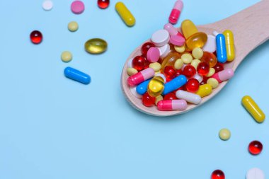 Renkli ilaç kapsülleri, tabletler ve mavi arka planda izole edilmiş tahta kaşıkta haplar. Beslenme takviyesi sağlık ürünleri. Metin için alanı kopyala.