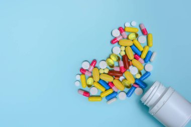 Renkli kapsülleri, vitaminleri, takviyeleri kalp şeklinde hapları olan beyaz bir şişe. Kalp hastalıklarının tedavisi için ilaçlar. Metin için alanı kopyala.