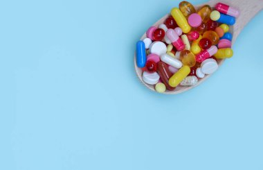 Renkli ilaç kapsülleri, tabletler ve mavi arka planda izole edilmiş tahta kaşıkta haplar. Beslenme takviyesi sağlık ürünleri. Metin için alanı kopyala.