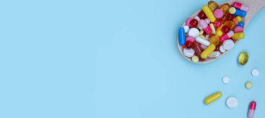 Renkli ilaç kapsülleri, tabletler ve mavi arka planda izole edilmiş tahta kaşıkta haplar. Beslenme takviyesi sağlık ürünleri. Metin için alanı kopyala. Banner
