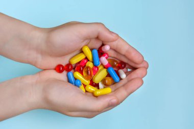 Çocuğun ellerinde bir sürü renkli vitamin, kapsül, takviye, hap var..