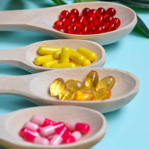 Four wooden spoons with multi-colored capsules,health supplements and vitamins with green leaves on a blue background.Supplemental and healthcare product, flat lay surface