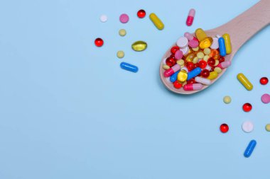 Renkli ilaç kapsülleri, tabletler ve mavi arka planda izole edilmiş tahta kaşıkta haplar. Beslenme takviyesi sağlık ürünleri. Metin için alanı kopyala.