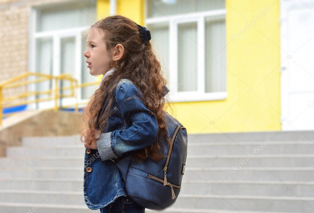 Beautiful sad schoolgirl with a backpack on the background of the school.Education concept. Back to school