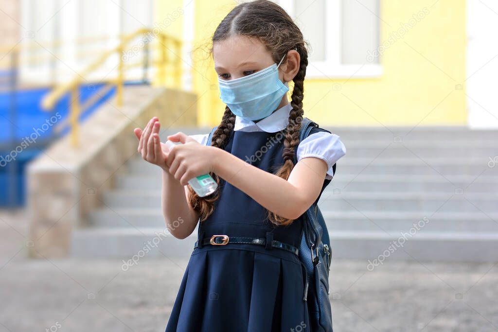 Portrait of schoo girl with surgical mask using hand sanitizer gel on the background of the school . Antiseptic, Hygiene and Healthcare concept.Back to school after pandemic .