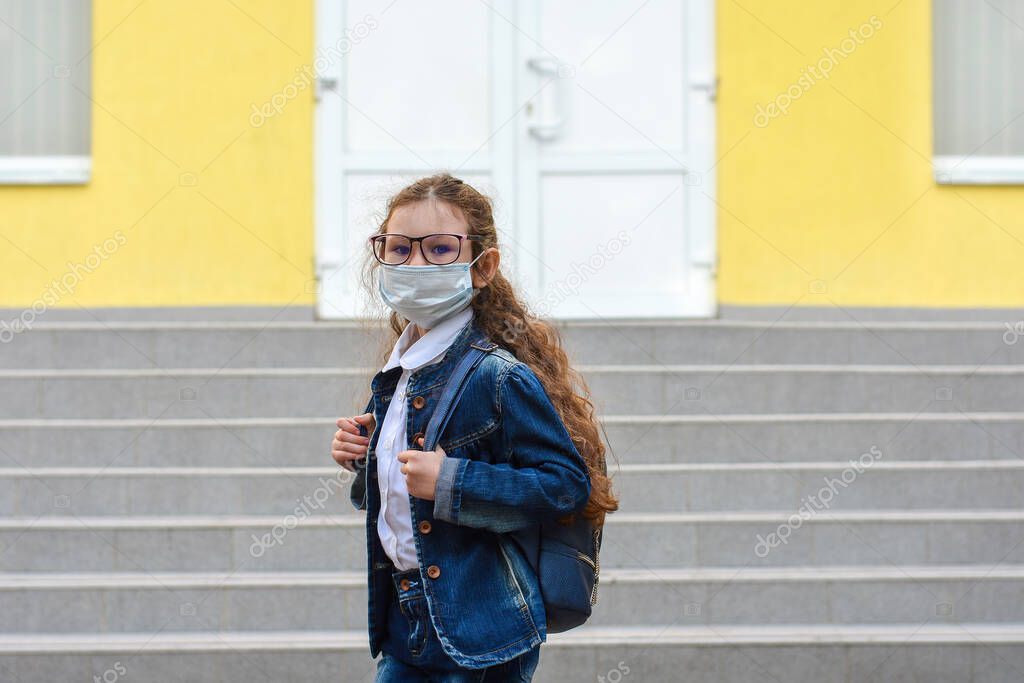 Back to school. Schoolgirl wearing medical face mask to health protection from influenza virus. Child going school after pandemic over.Portrait of a schoolgirl on the background of the school