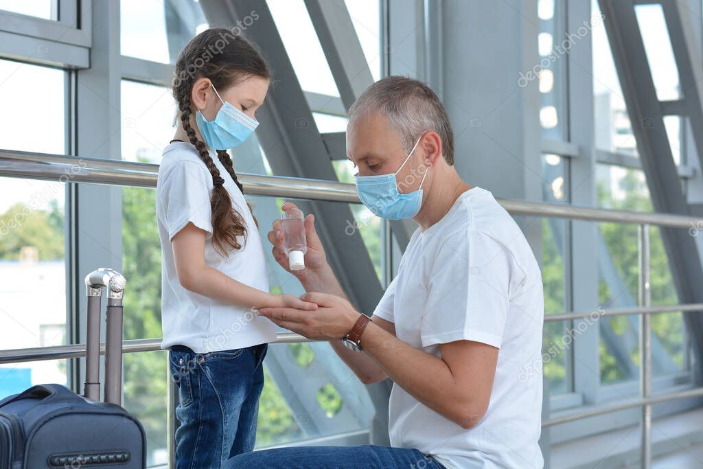 Father and daughter wearing protective medical masks use disinfectant at the airport or mall.Virus and illness protection, hand sanitizer in public crowded place.