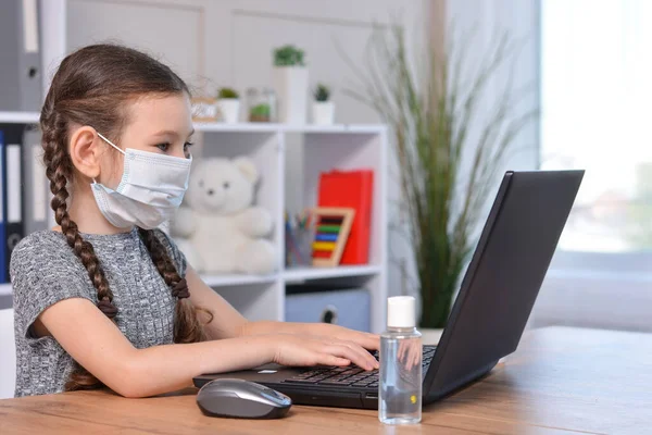Schoolgirl in a medical mask and headphones with a microphone doing homework at home or studying in class at a lesson at school.Student safety after covid-19 pandemic. Back to school.Distance learning