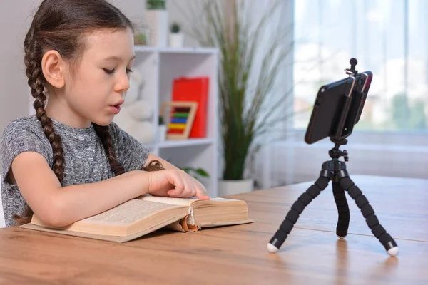 Distance learning online education.Schoolgirl is reading a book.Record video on a phone that is on the tripod