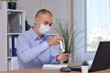 Maskeli bir iş adamı Covid-19 'a karşı el yıkama jeli kullanıyor. Ofiste ve evde yeni bir normal. Virüs ve hastalık koruması, kalabalık bir yerde el dezenfektanı.