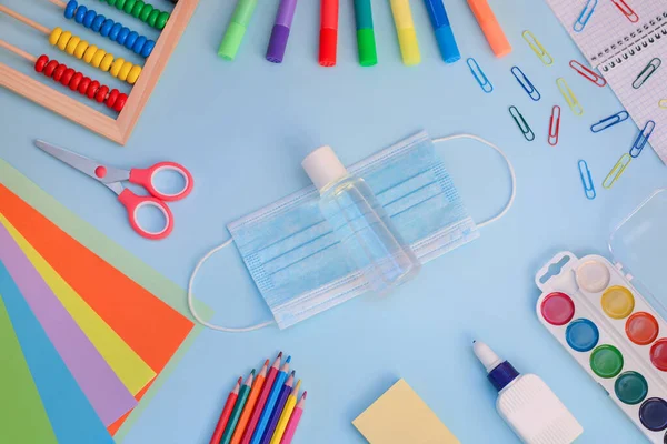 School supplies with medical mask and sanitizer on blue background.Back to school after coronavirus. Protection of schoolchildren and students from the coronavirus covid-19. Flat lay, top view.