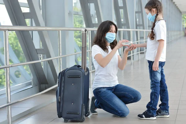 Koruyucu tıbbi maskeler takan anne ve kız havaalanında ya da alışveriş merkezinde dezenfektan kullanıyor. Virüs ve hastalık koruması, kalabalık bir yerde el dezenfektanı..