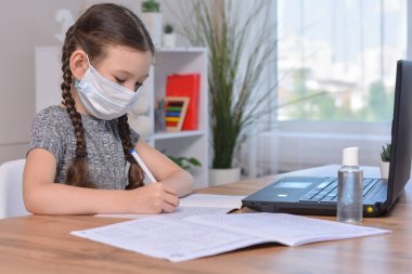 Tıp maskeli bir öğrenci ödevini evde dizüstü bilgisayarda ya da okulda bir derste yapıyor. Covid-19 salgınından sonra öğrenci güvenliği. Okula dönüyorum. Mesafe öğreniyorum..